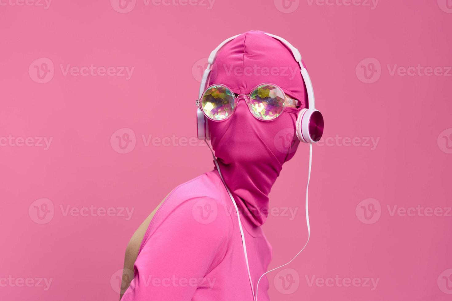 Creative fan art photo of a young female cyberpunk blogger on a pink background wearing a pink full-face mask with glowing round glasses and headphones