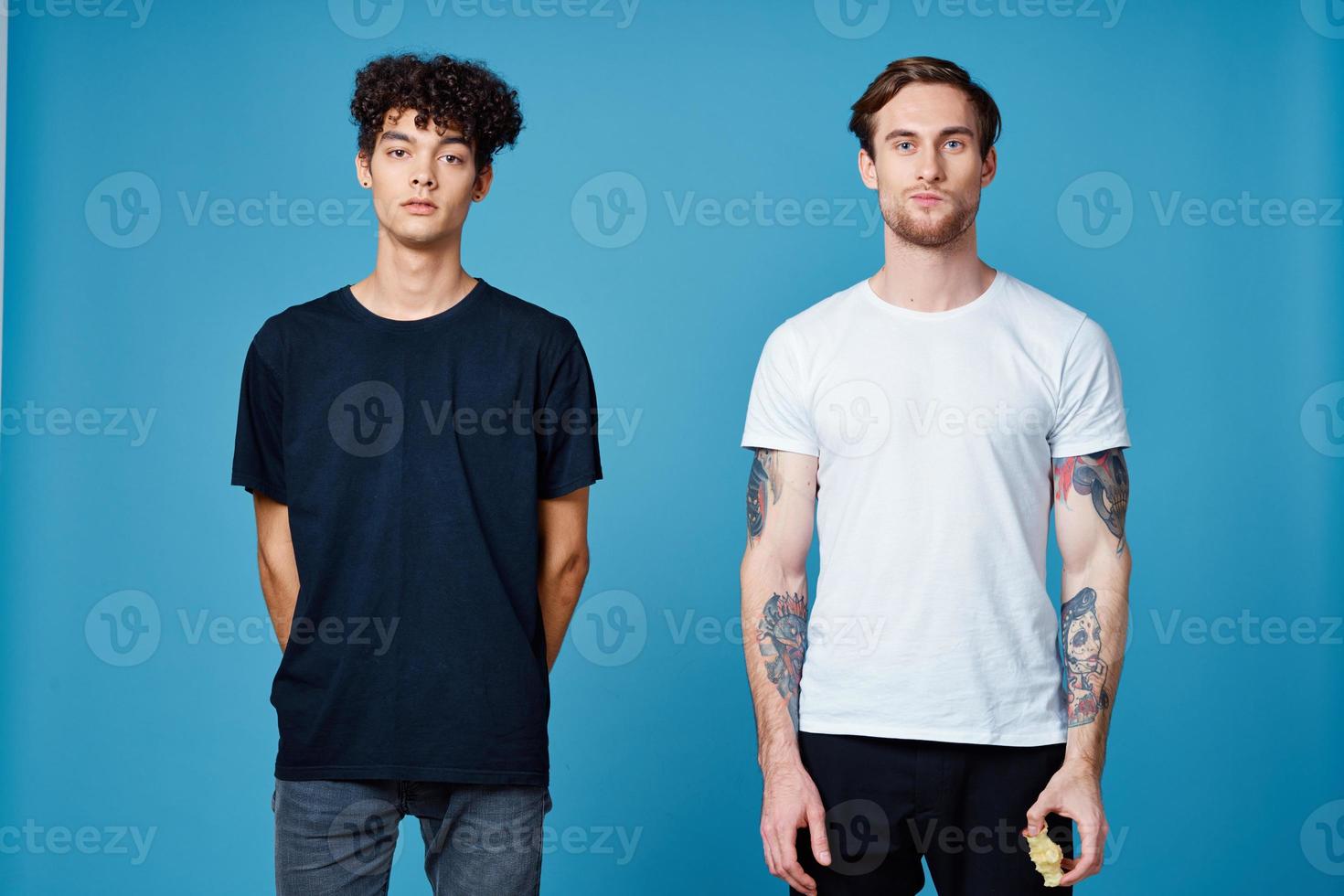 curly guy in a black t-shirt and a man with a tattoo on a blue background friends chatting photo