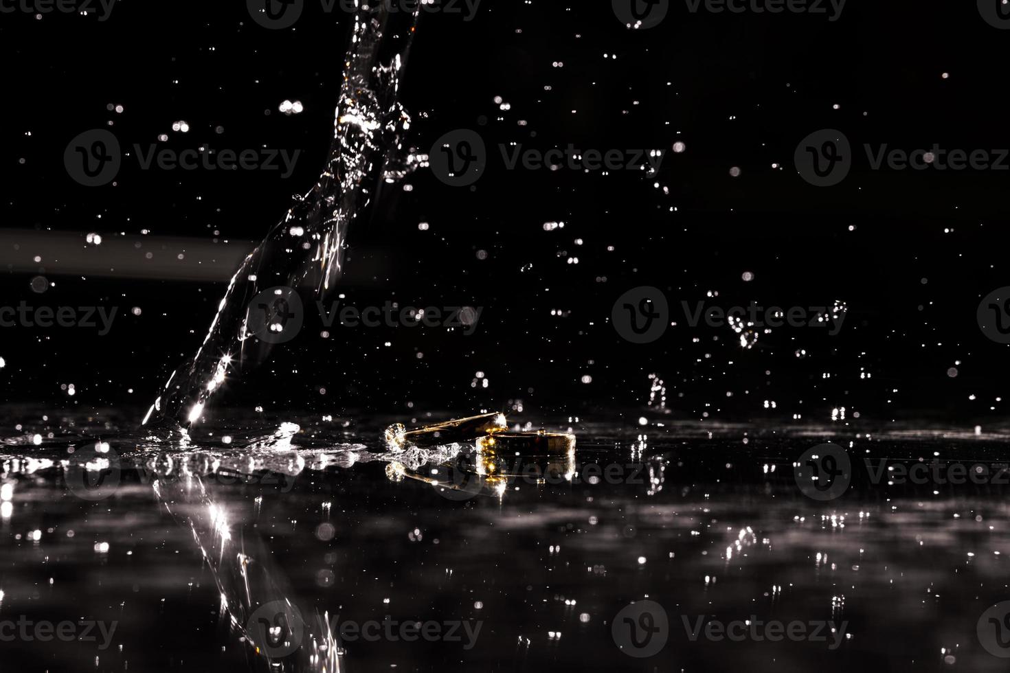 hermosa Boda anillos de el novia y novio en un negro antecedentes. gotas de agua goteo en dorado anillos un fascinante vista. foto