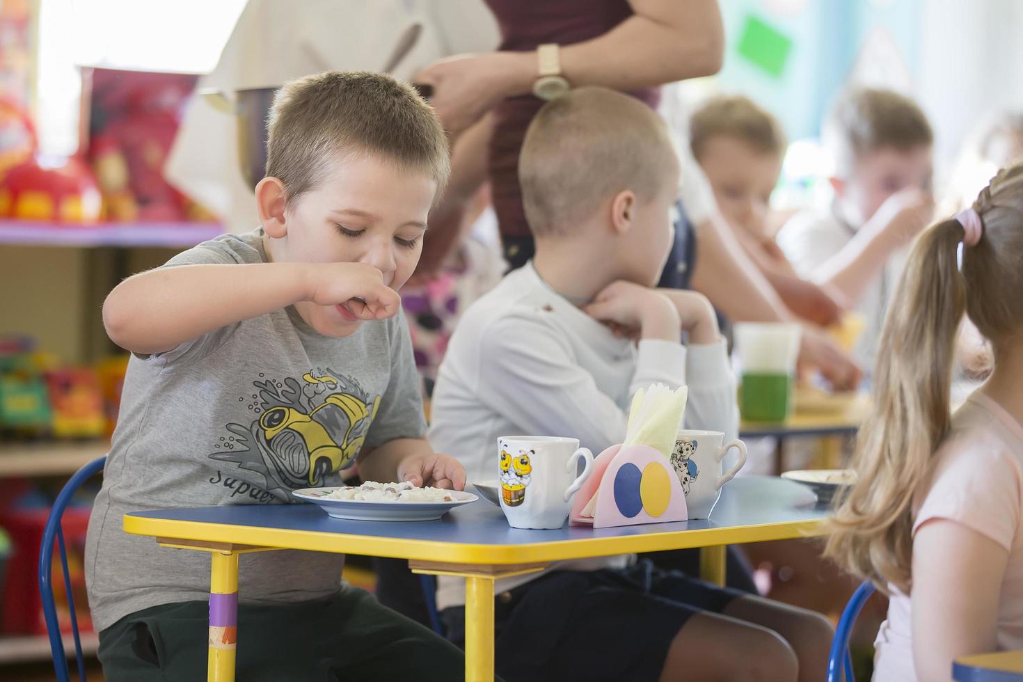 Children eat in kindergarten. Boy with a spoon and a plate at the table photo