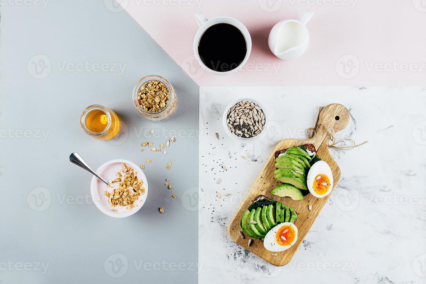 Healthy Breakfast concept. Sandwich with avocado and boiled eggs, yogurt with granola, cup of coffee over tricolor stylish background, top view, copy space, flat lay photo