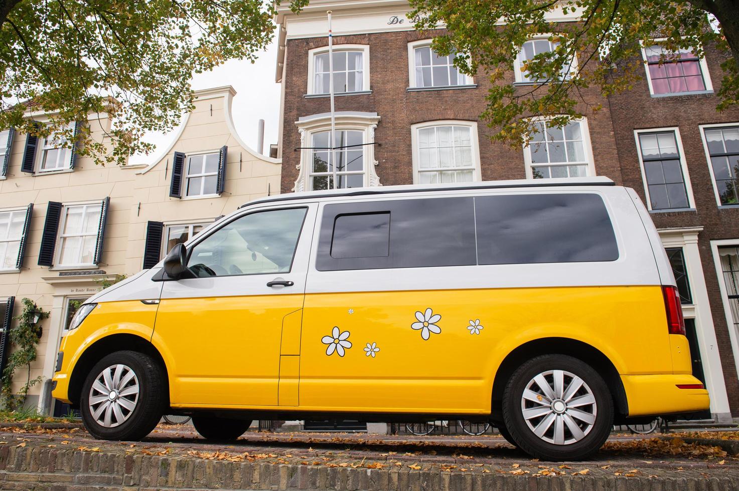 Yellow van minibus with painted chamomile flowers stands on the edge of the sidewalk near the canal photo