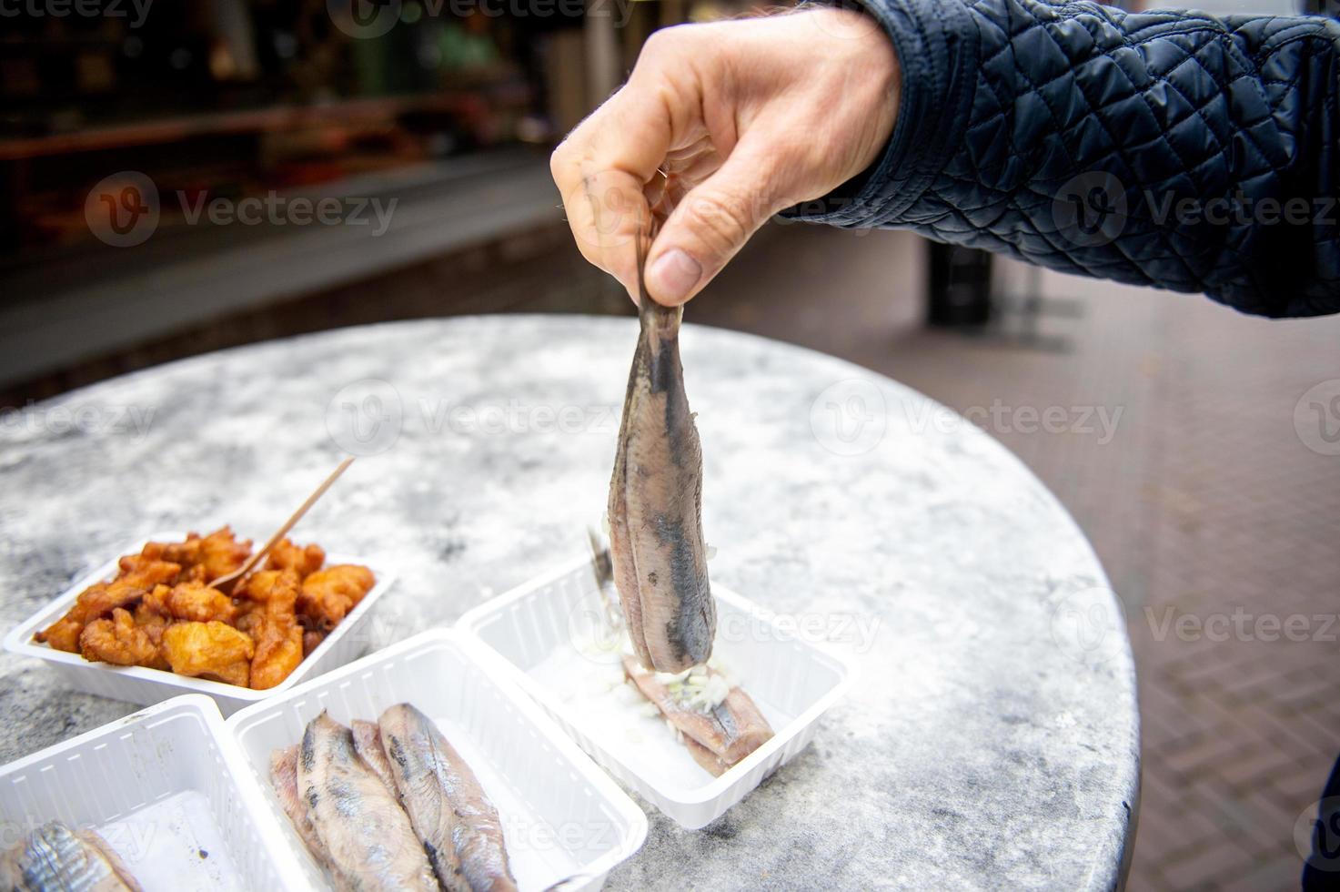 Food from a fish restaurant in Holland, eat on the street. Hold herring with onions by the tail. photo