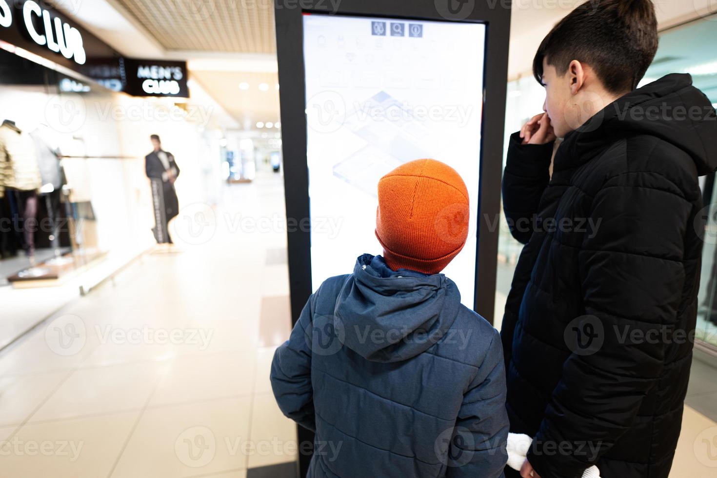 Two brothers customers standing near electronic information desk looking for boutique or shop location in the big mall photo