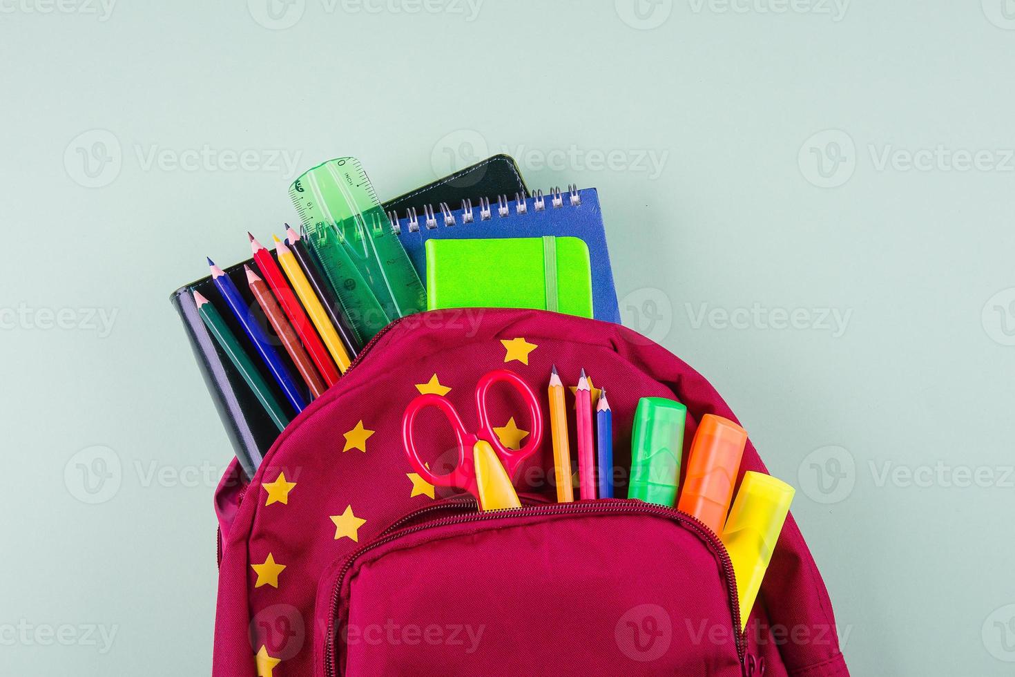 espalda a colegio concepto. rojo mochila con diferente vistoso papelería en pastel verde antecedentes. foto