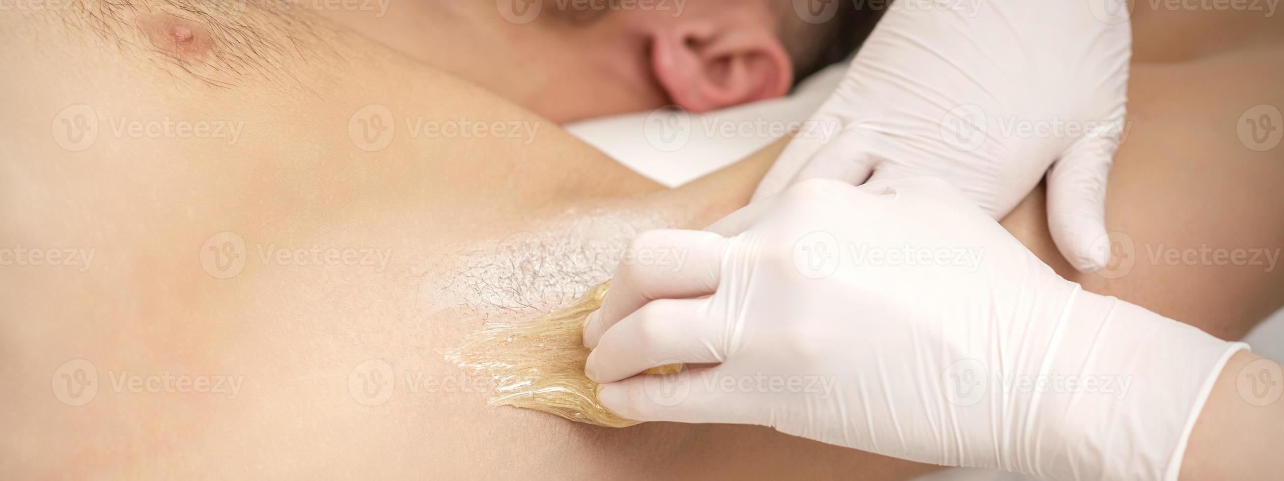 Beautician waxing young male armpit photo