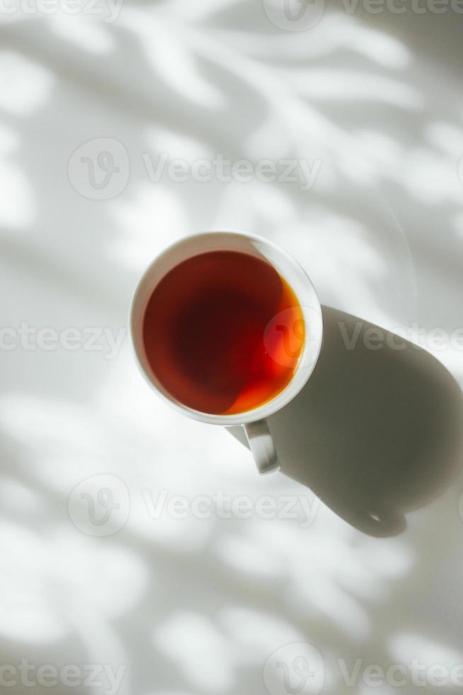 White cup of tea on abstract background of natural curtain shadow falling on white table. photo