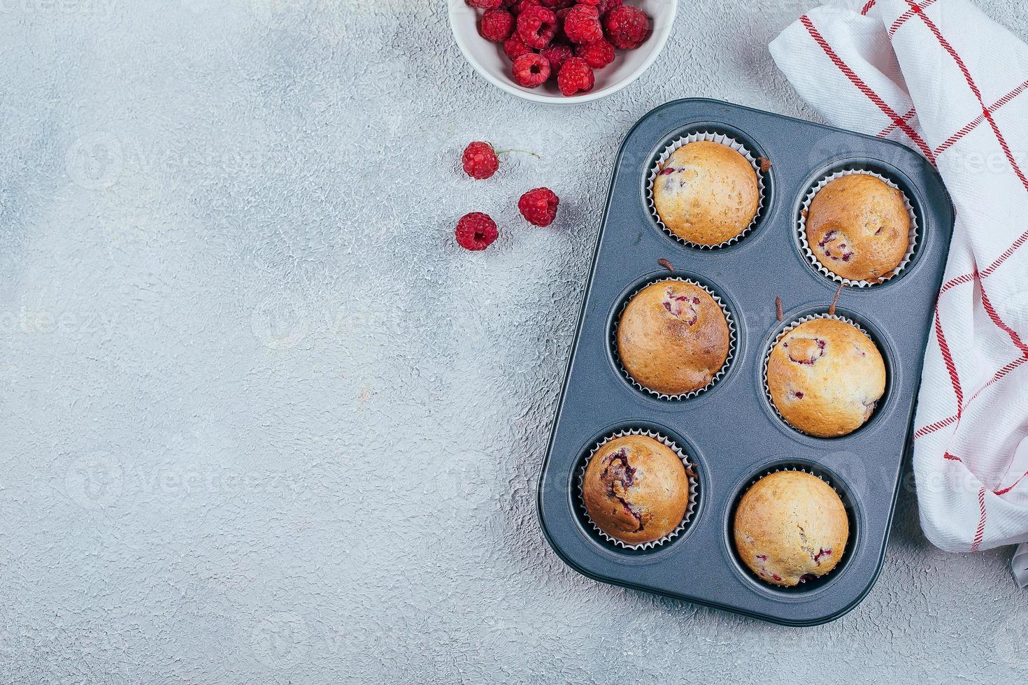 Baked Raspberry Muffins on a cooling rack on blue concrete table background. Top view, copy space. photo