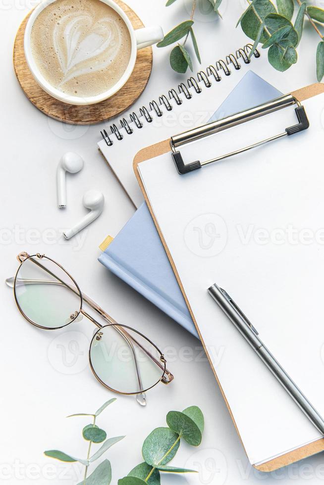 Modern white office desk table with coffee, notebook and other supplies. photo