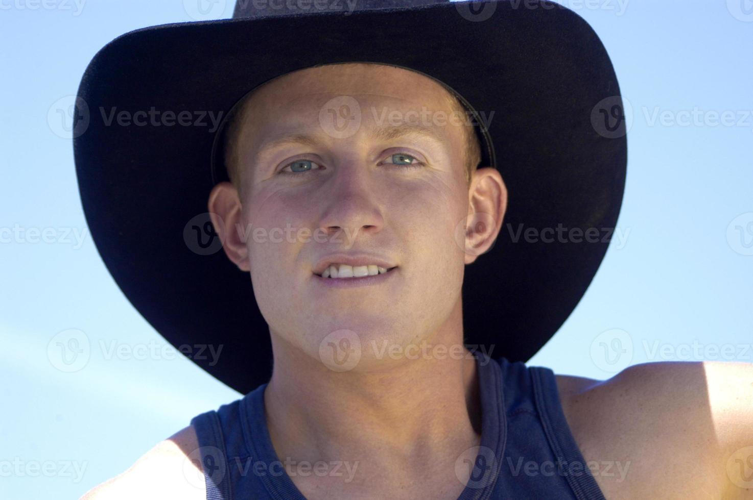 A young, blond cowboy is depicted in close-up, with the only background being the sky. photo