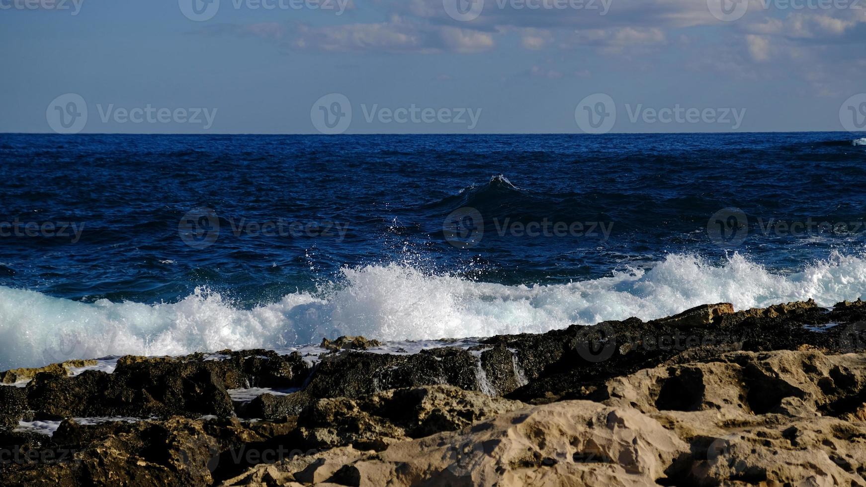 Blue sea wave and white foam and splash. Stone beach on island of Malta, no sandy beach. Summer holiday border frame concept. Tropical island vacation backdrop. Tourist travel banner design template. photo