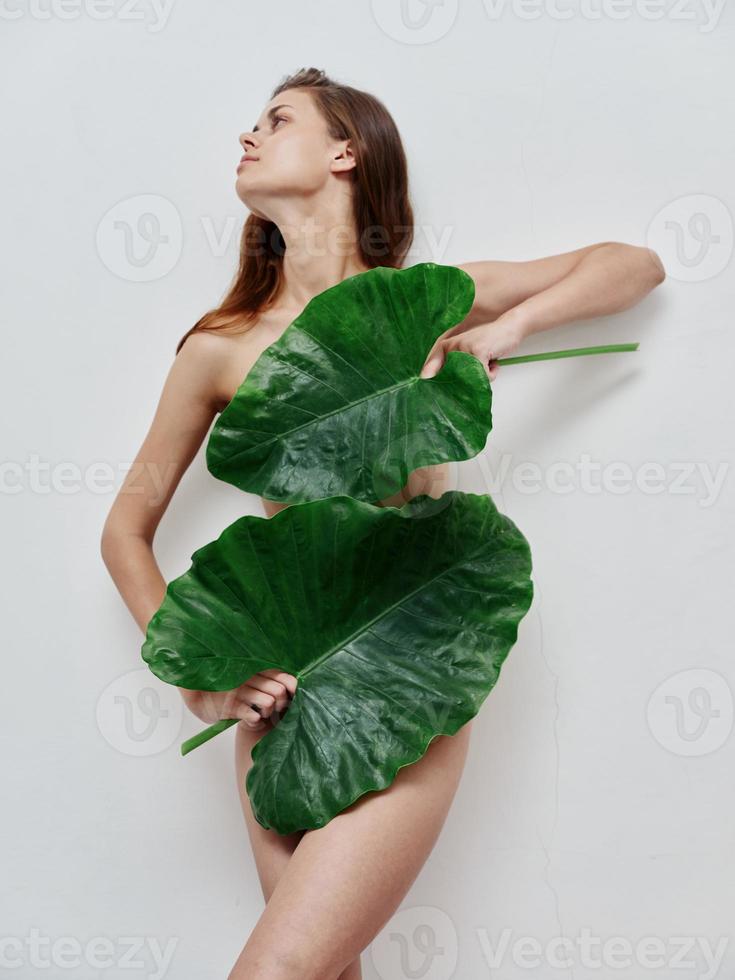 woman with naked body and green leaves light background photo