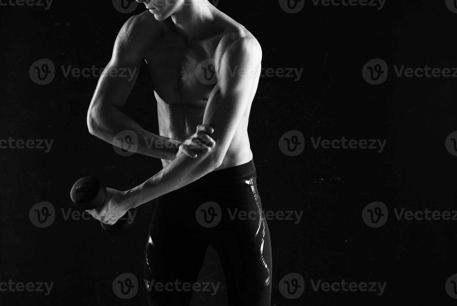 sporty man with dumbbells in hands pumping up muscles exercises dark background photo