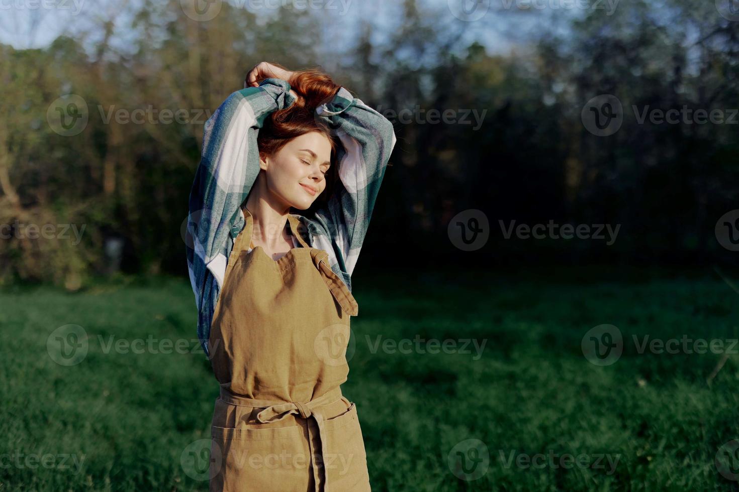 Portrait of a woman with a beautiful smile in her work clothes and apron in nature, enjoying relaxation after work in the sunset sunlight photo