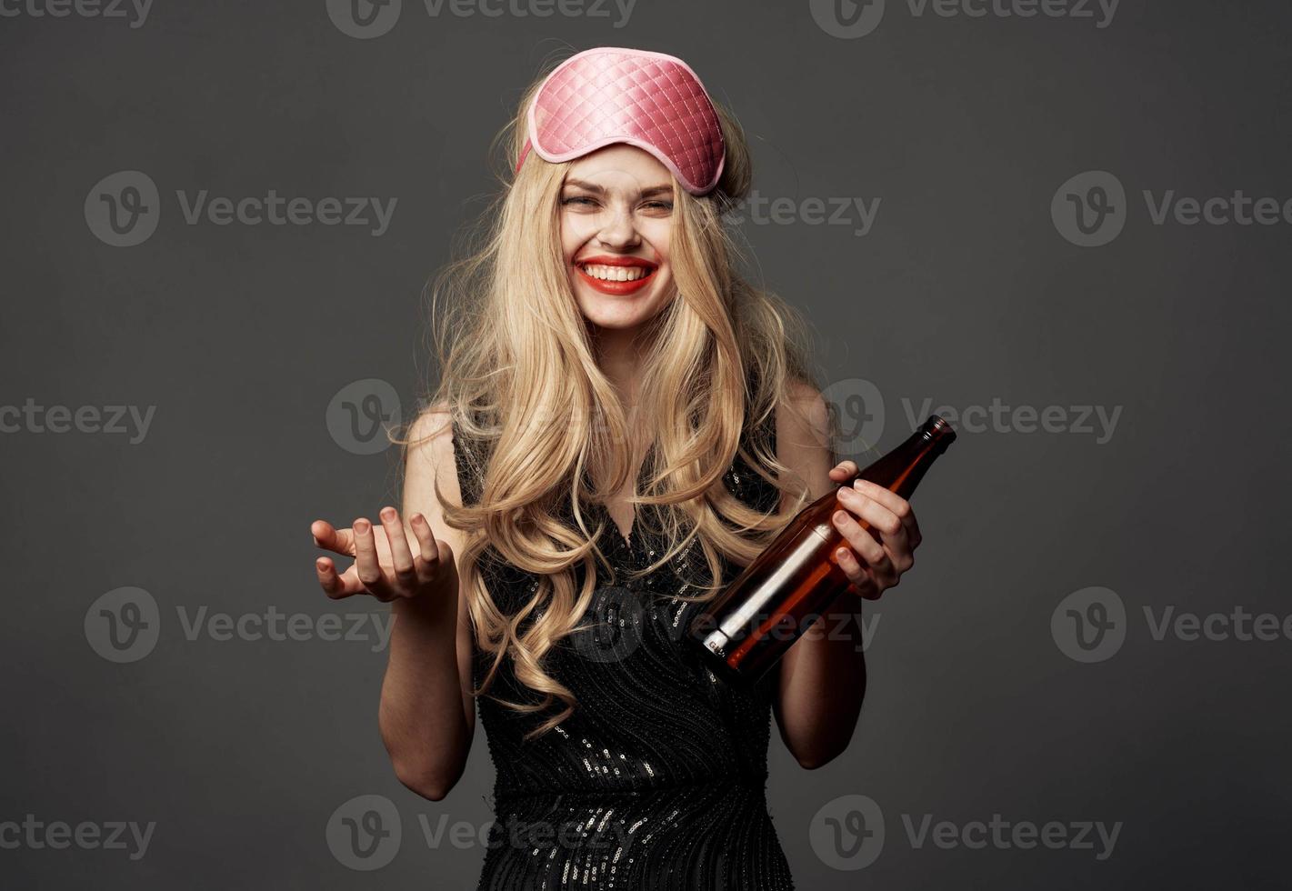 Woman with a bottle of beer on a gray background holidays sleep mask on her head photo