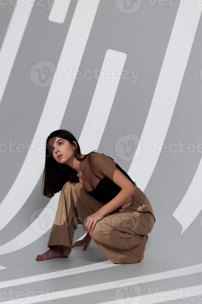 a woman in beige trousers sits on the floor with her legs apart and a falling shadow In a bright room photo