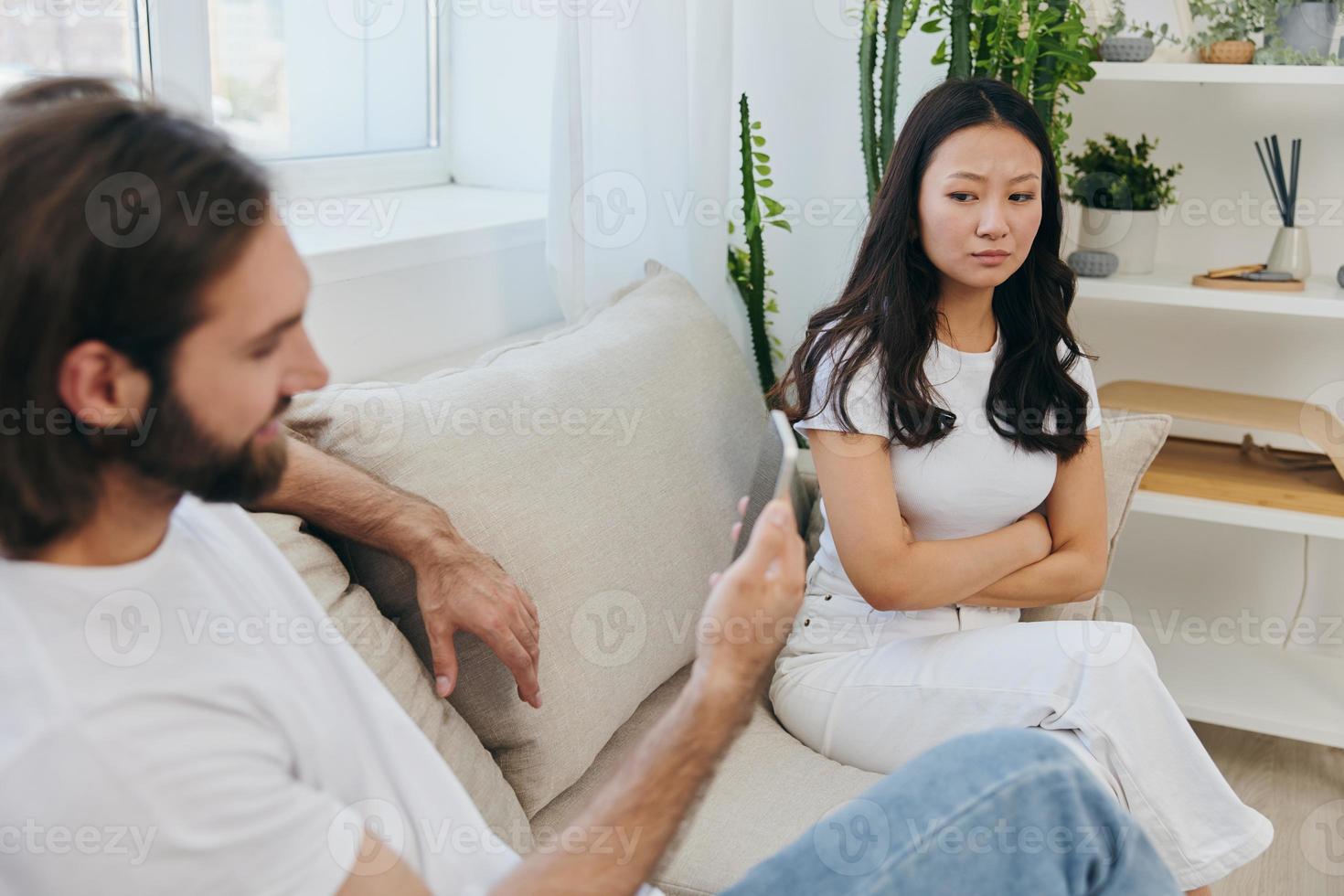 A man looks at the phone screen during an argument with his girlfriend. The angry and hurt woman looks in his direction and is sad. Family discord at home, phone addiction photo