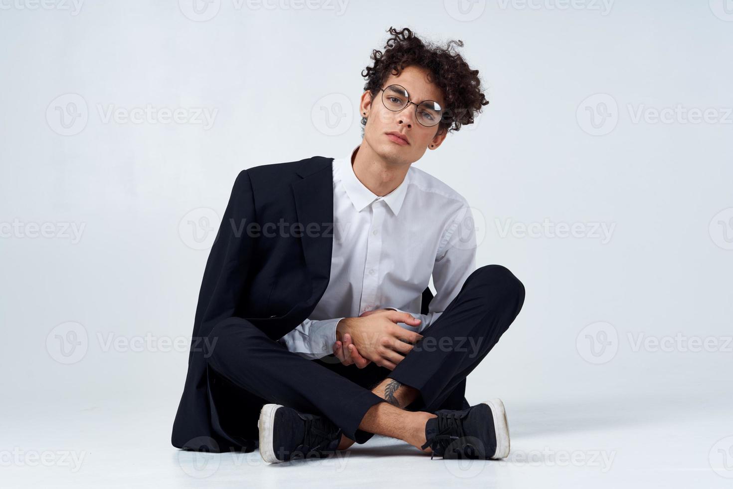 a guy in a shirt, trousers and sneakers on the floor in a bright room and a jacket on his shoulder photo