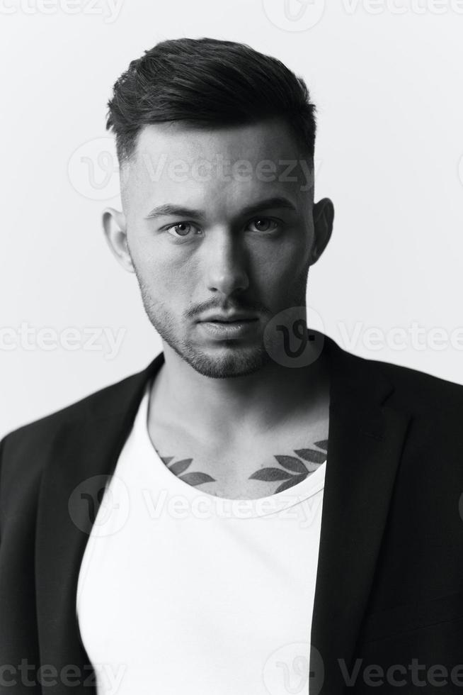 Modelling snapshots. Closeup portrait of self-confident attractive handsome muscular guy man in jacket looks at camera sitting on chair in white studio background. Black and White concept. Copy space photo