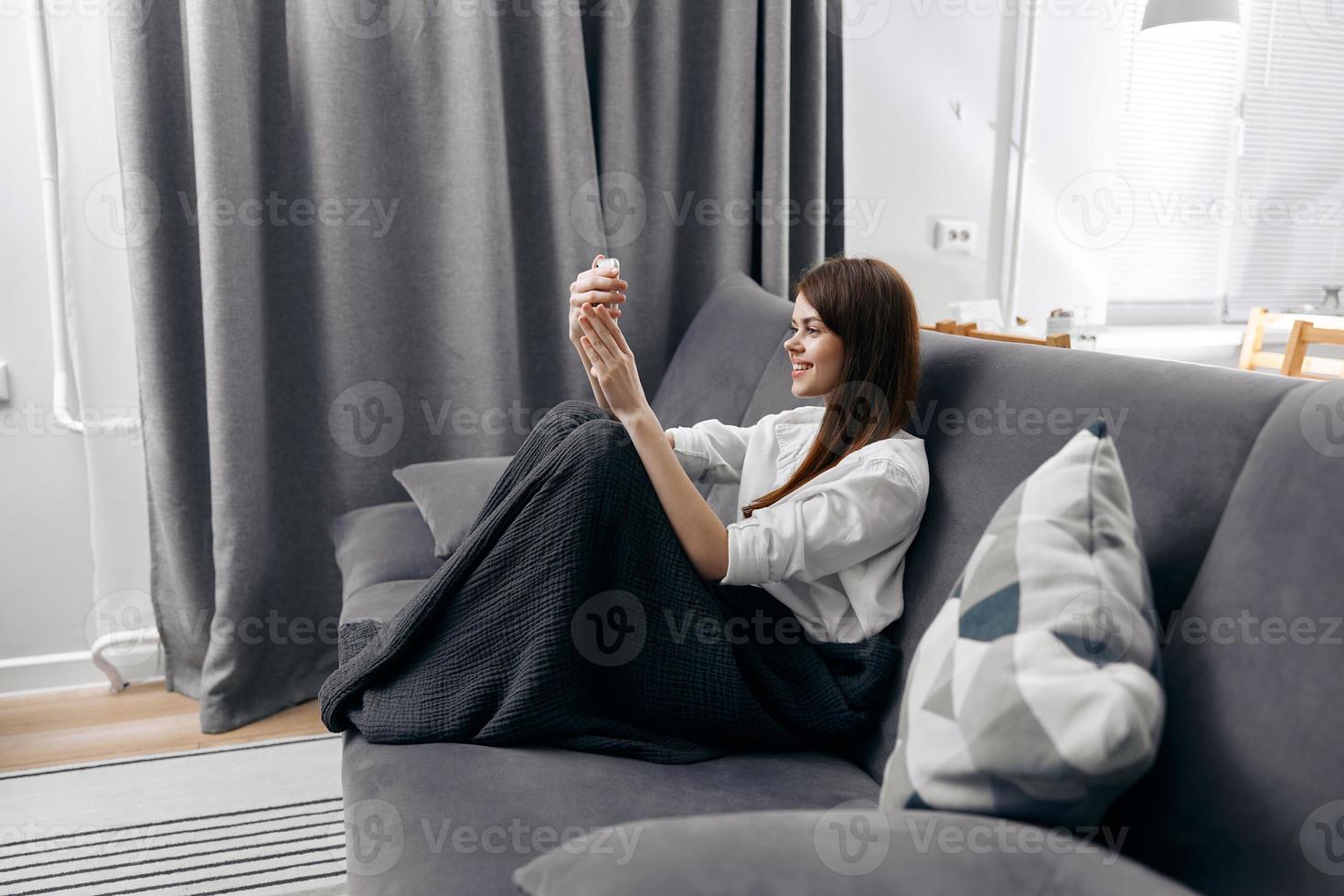 happy woman on the sofa with a blanket on her lap and a mobile phone in her hand photo