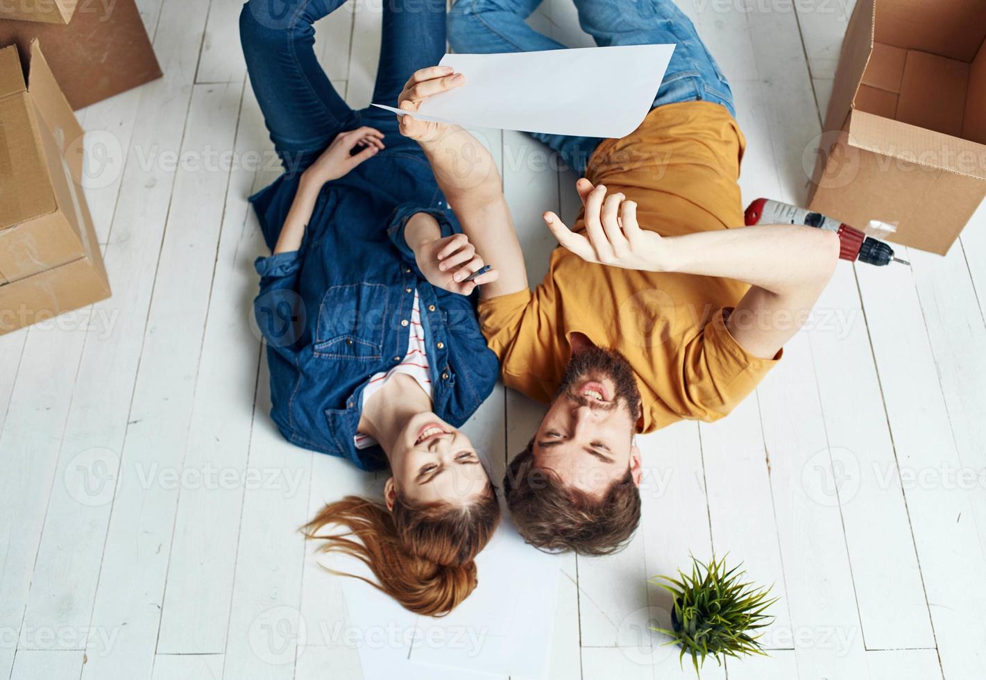 man and woman with boxes around lie on the floor moving flower in a pot repair work photo