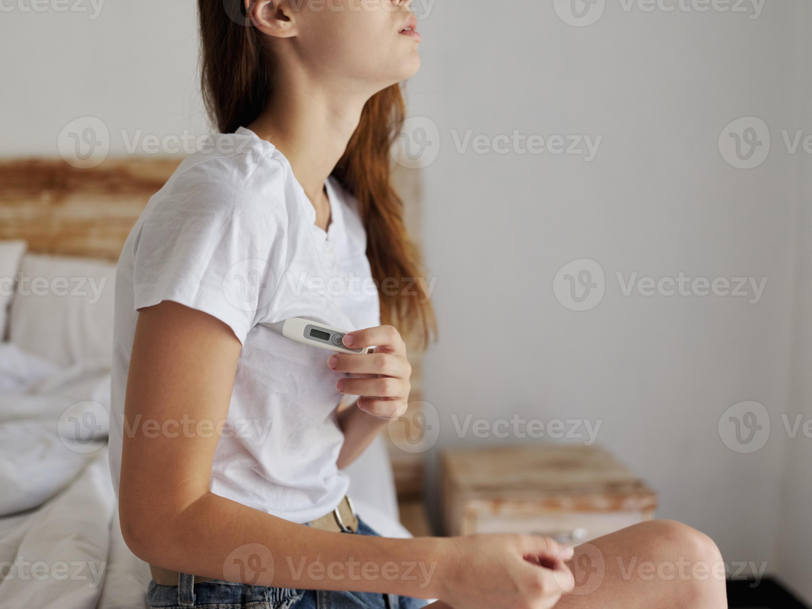 woman sitting on bed with thermometer armpit checking temperature