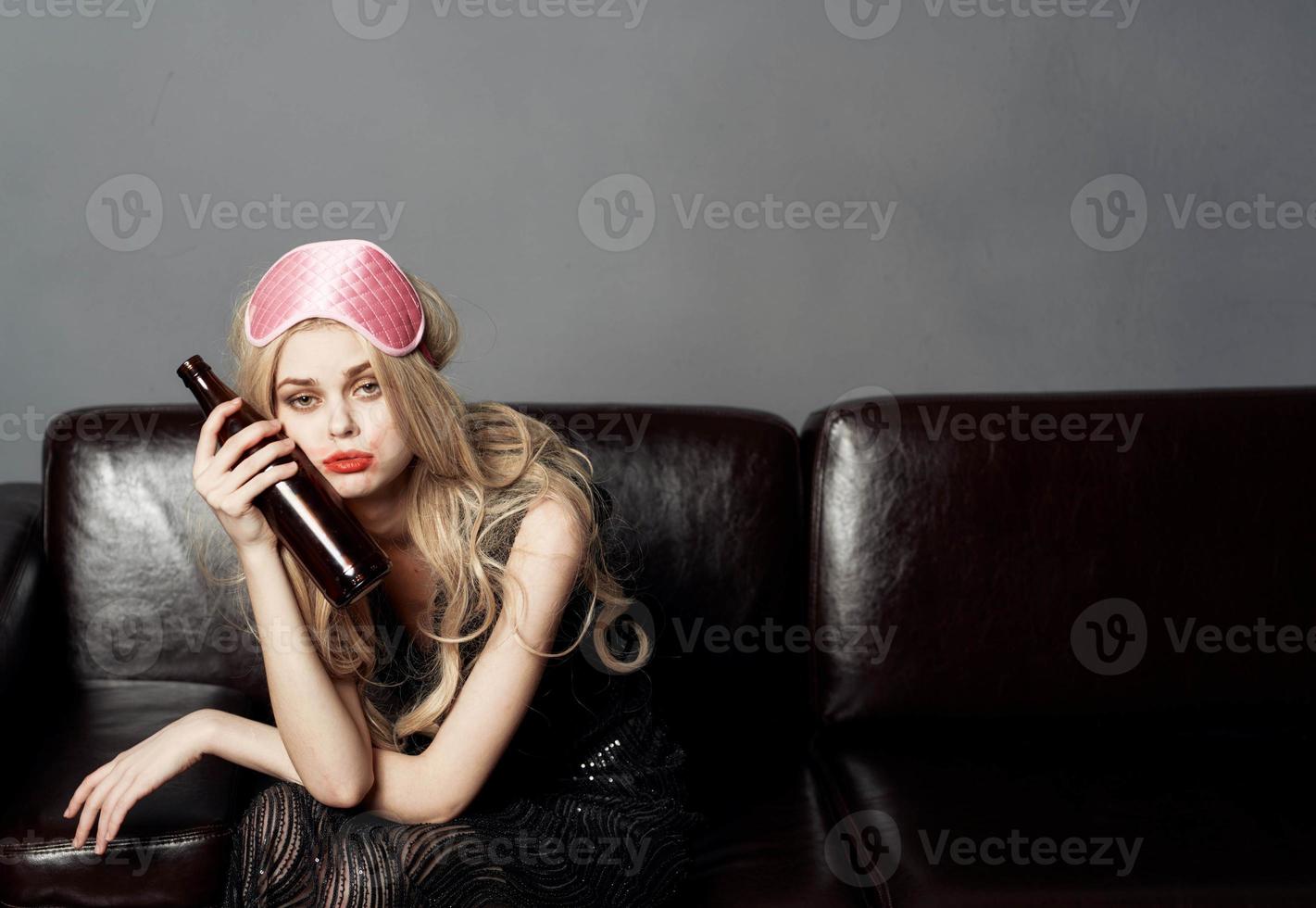 woman with bottle of beer on sofa alcohol addiction sleep mask on head photo