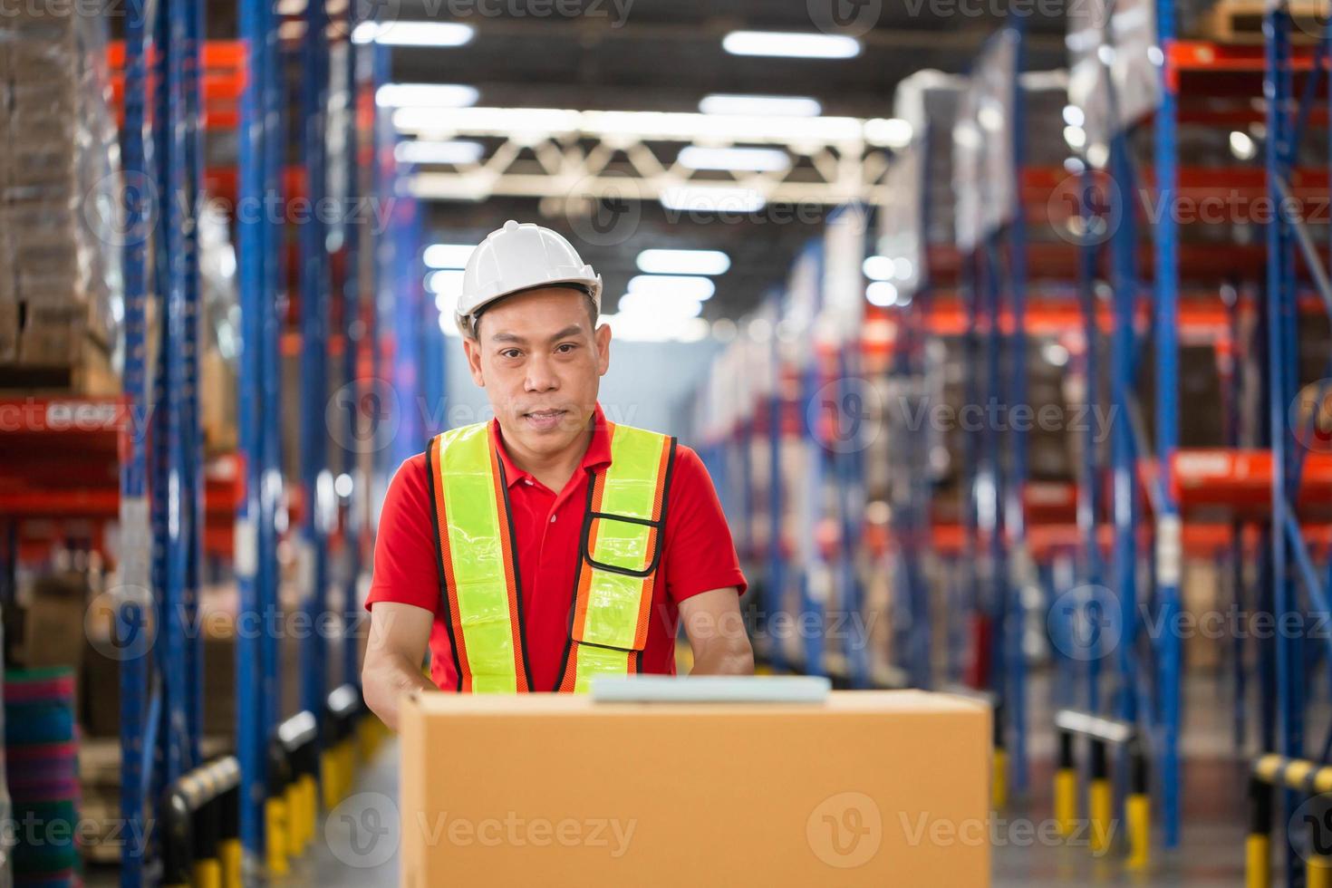 Cheerful warehouse worker checking inventory and working in warehouse, Worker man using hand pallet jack unloading package boxes at factory warehouse photo