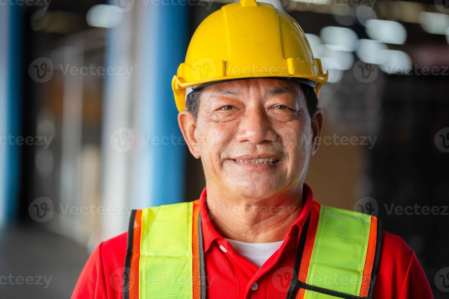 retrato de trabajador vistiendo casco de seguridad y la seguridad chaleco en pie en el depósito, alegre hombre mirando a cámara con borroso antecedentes foto