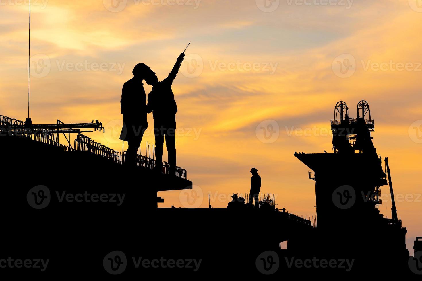 Silhouette of Engineer and foreman worker checking project at infrastructure construction site, construction site at sunset in evening photo