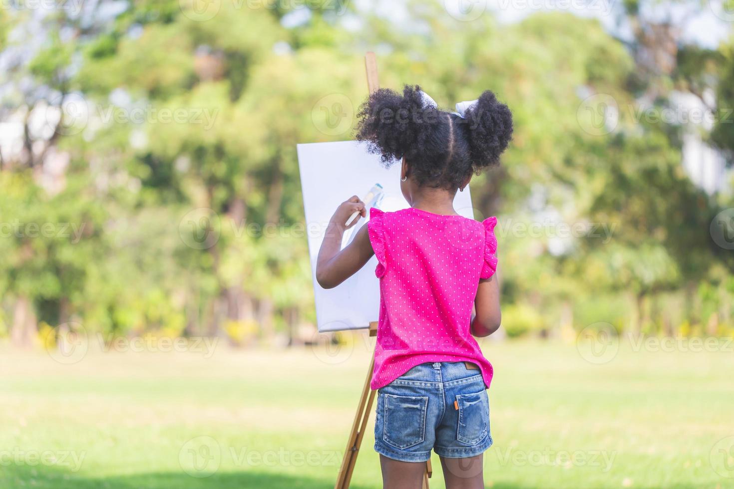 espalda ver de niño niña pintura en lona en el jardín, contento niño niña dibujo un imagen al aire libre foto