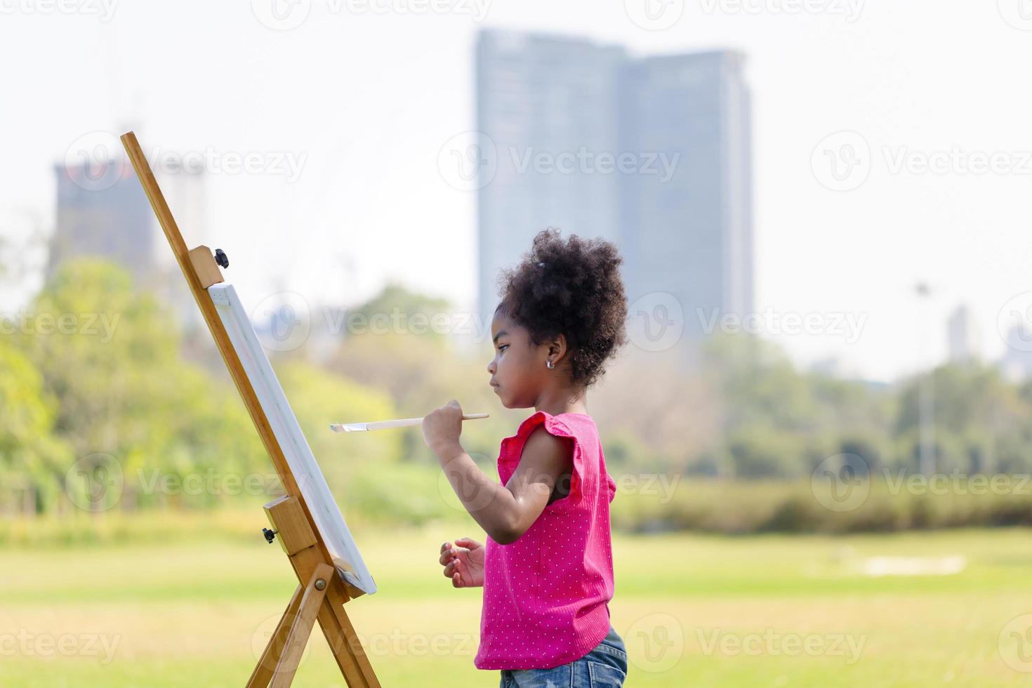 niño niña pintura en lona en el jardín, contento niño niña dibujo un imagen al aire libre foto