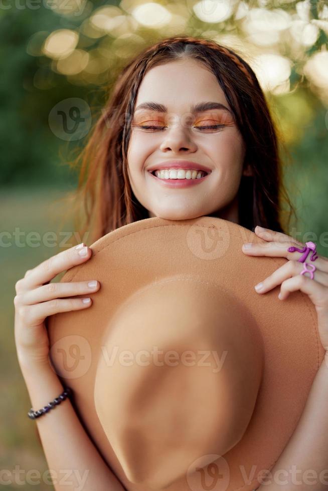 Young hippie woman holding a hat and smiling sincerely while looking at the camera in nature in the fall photo
