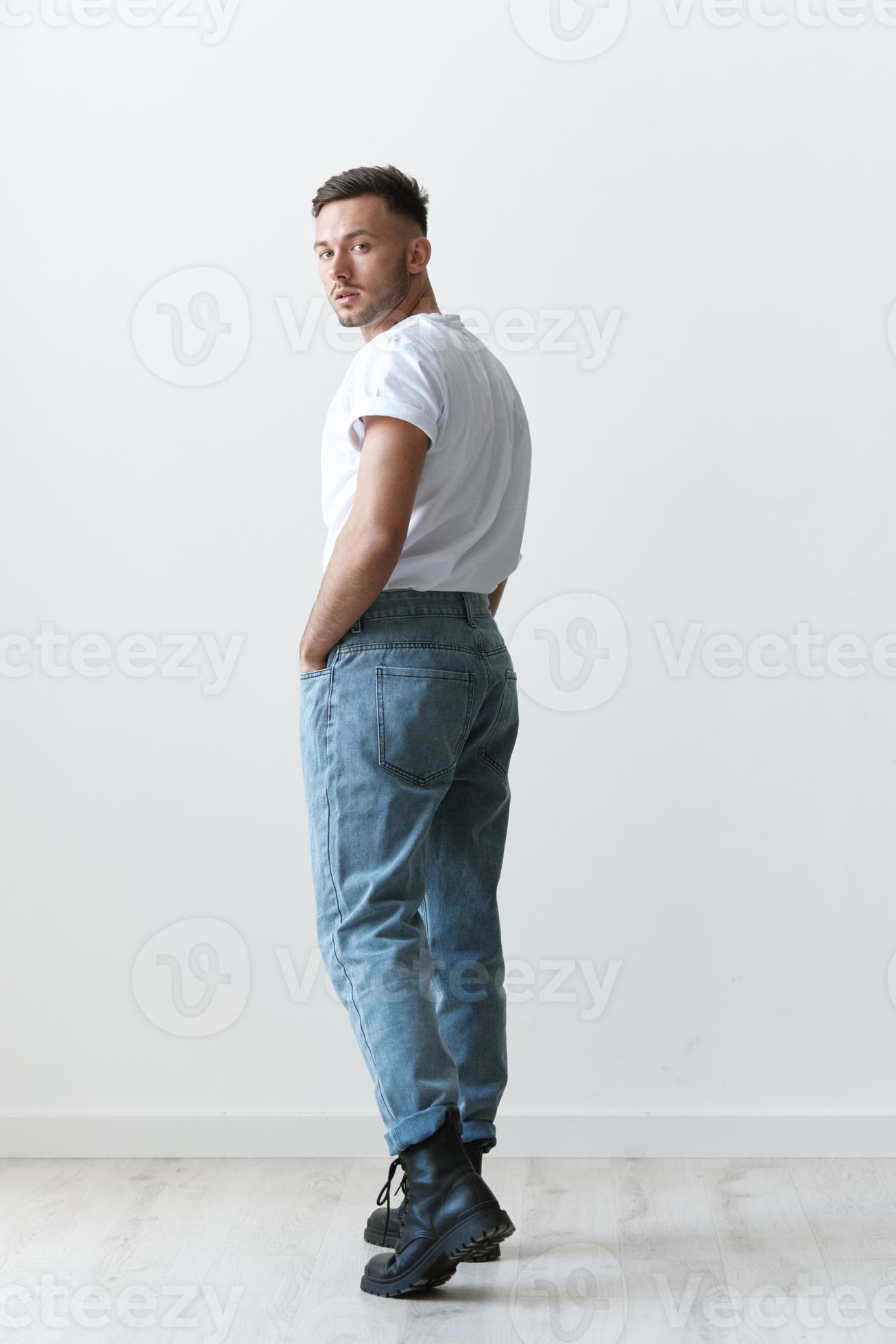 Full body view from the back shot of handsome serious tanned man guy in  basic t-shirt looks at camera posing on white background. Fashion Style New  Collection Offer. Copy space for ad.