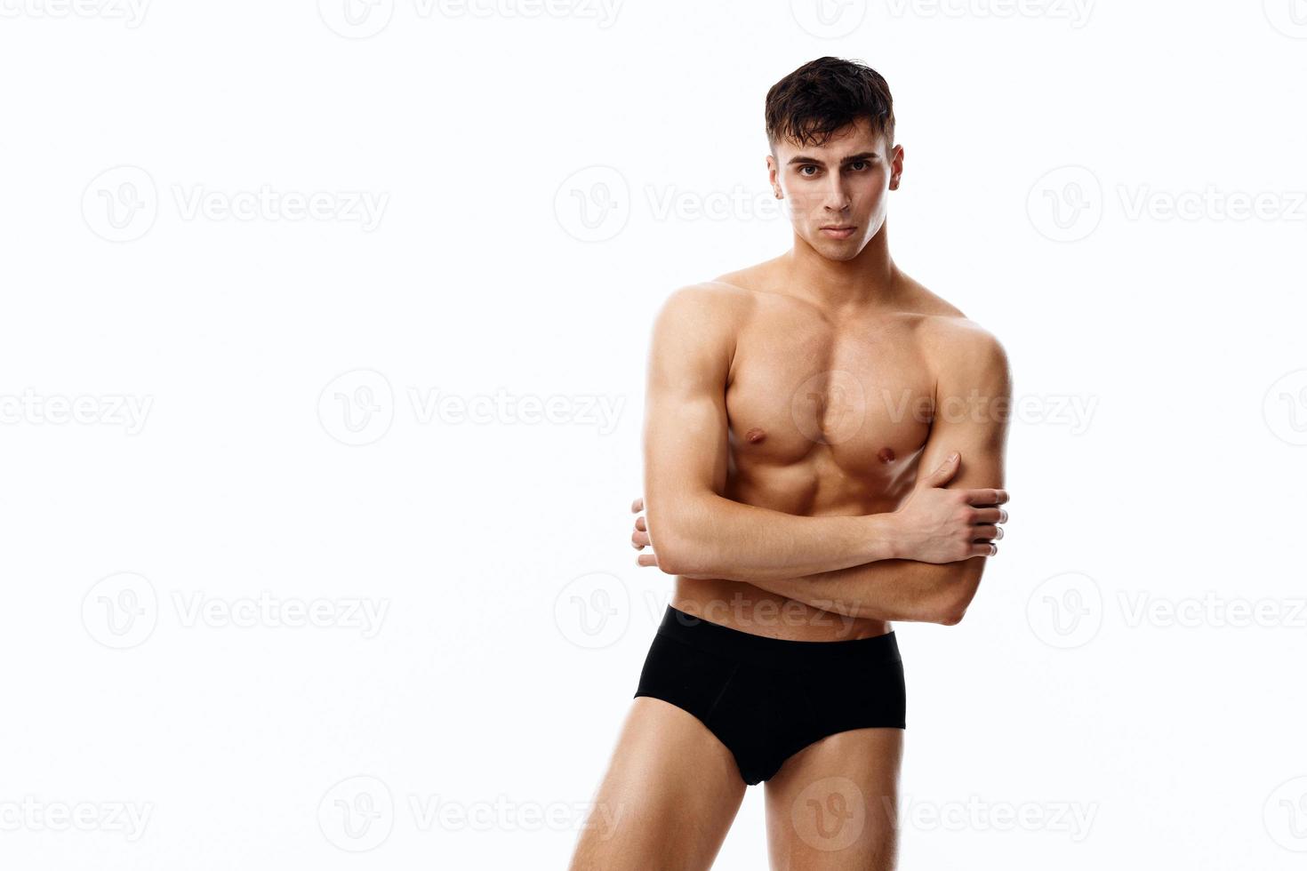 nude man in black panties holds his hands on his chest on a light background model photo