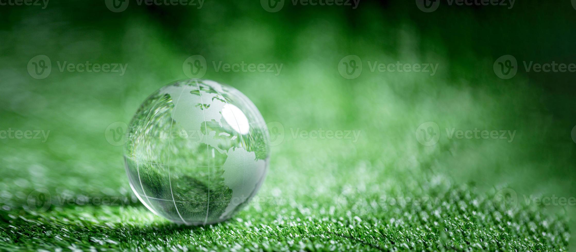 Close up of crystal globe resting on green grass with blur nature background, earth day or world environment day concept. Green world and sustainable conservation of forest resources. photo