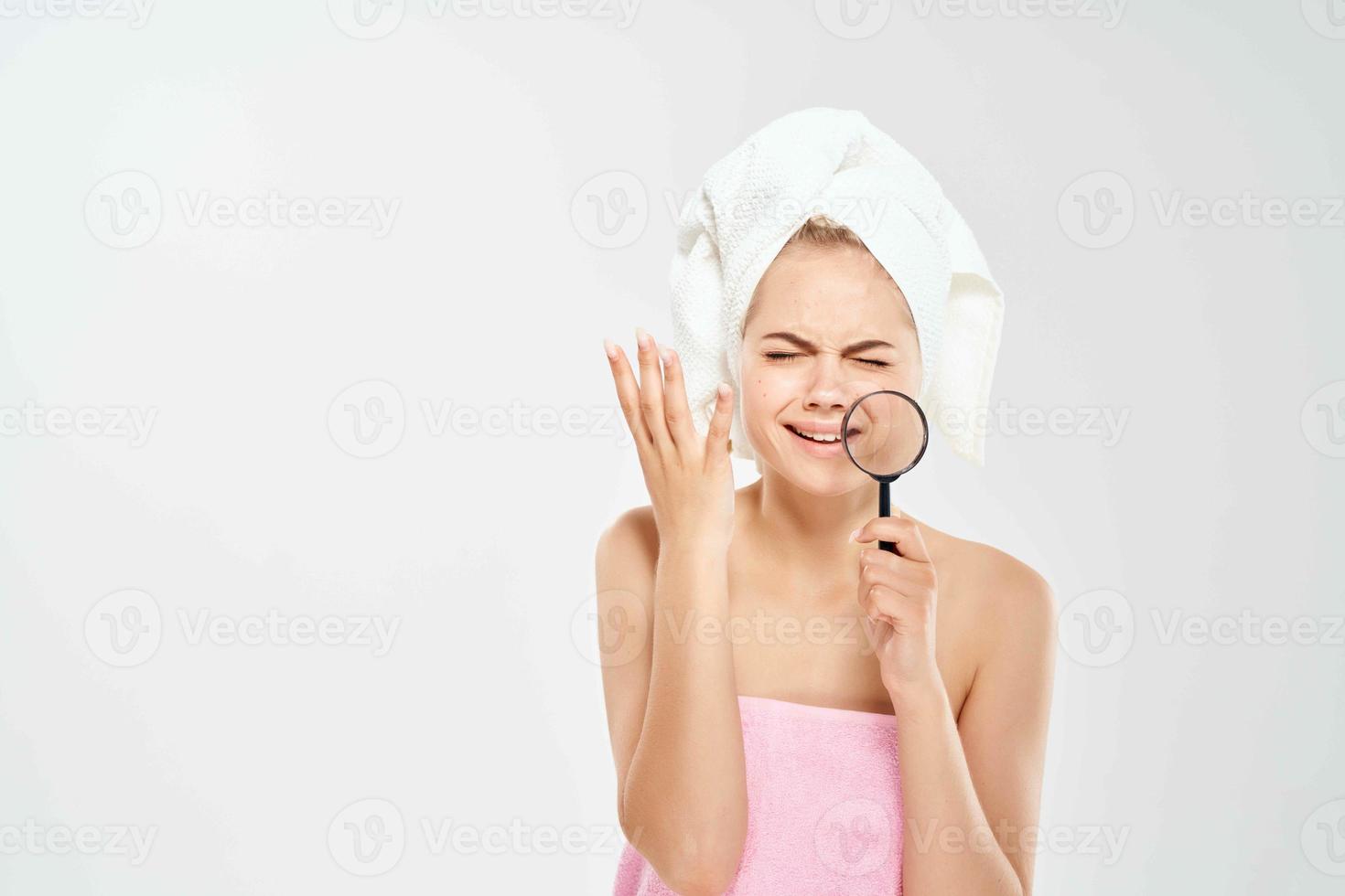woman with a towel on her head holds a magnifying glass near face acne photo