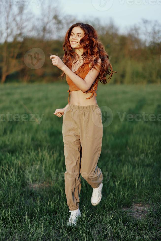 A woman works out and runs through the field in the park with a smile in a good mood looking at the beautiful summer nature around her photo