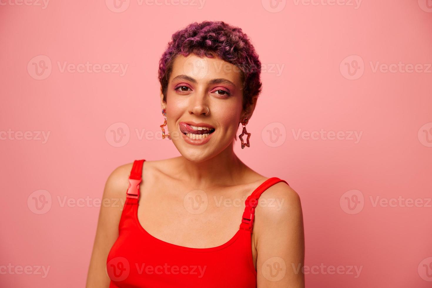 Fashion portrait of a woman with a short haircut of purple color and a smile with teeth in a red top on a pink background happiness photo
