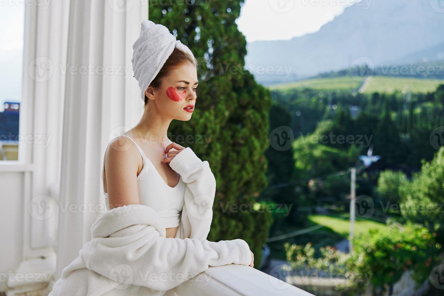 Sensual and beautiful woman with a towel on his head patches on his face stands on the balcony Perfect sunny morning photo