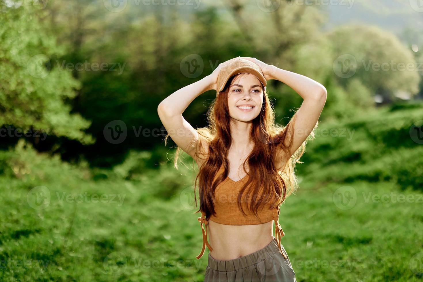A young woman with an athletic body walks in a summer green park in nature. Sunset sunlight illuminates her red hair photo
