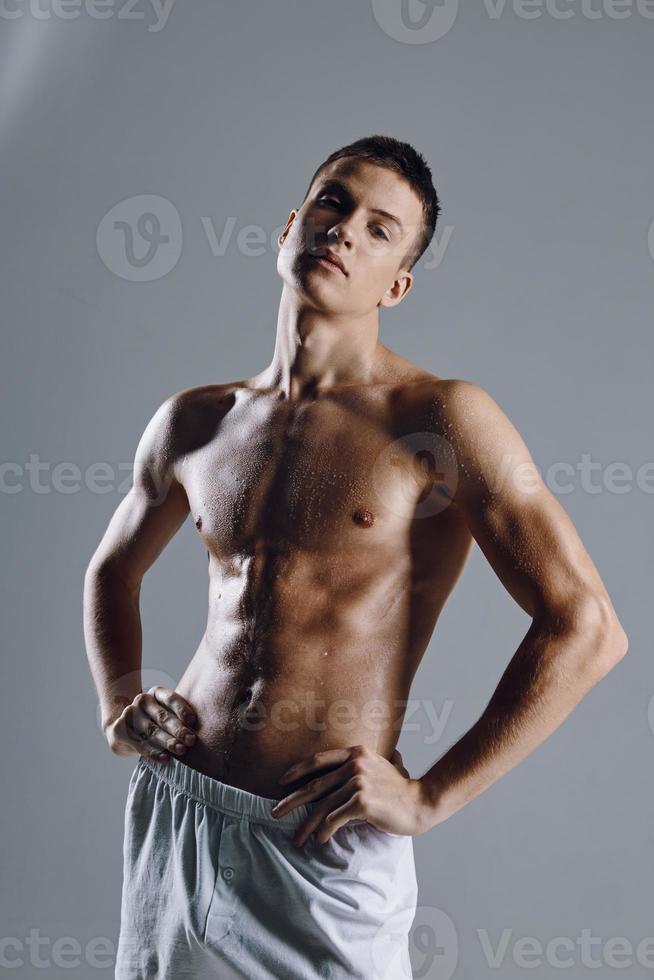 semidesnudo atleta en blanco pantalones cortos participación manos en el cinturón en un gris antecedentes foto