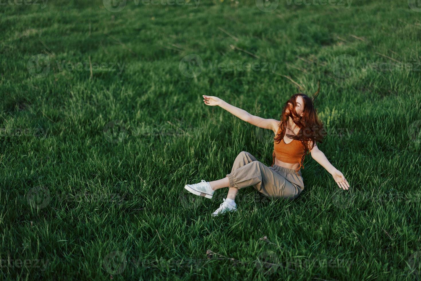 Young woman playing games in the park on the green grass spreading her arms and legs in different directions falling and smiling in the sunlight of summer, a lifestyle of life and youth photo