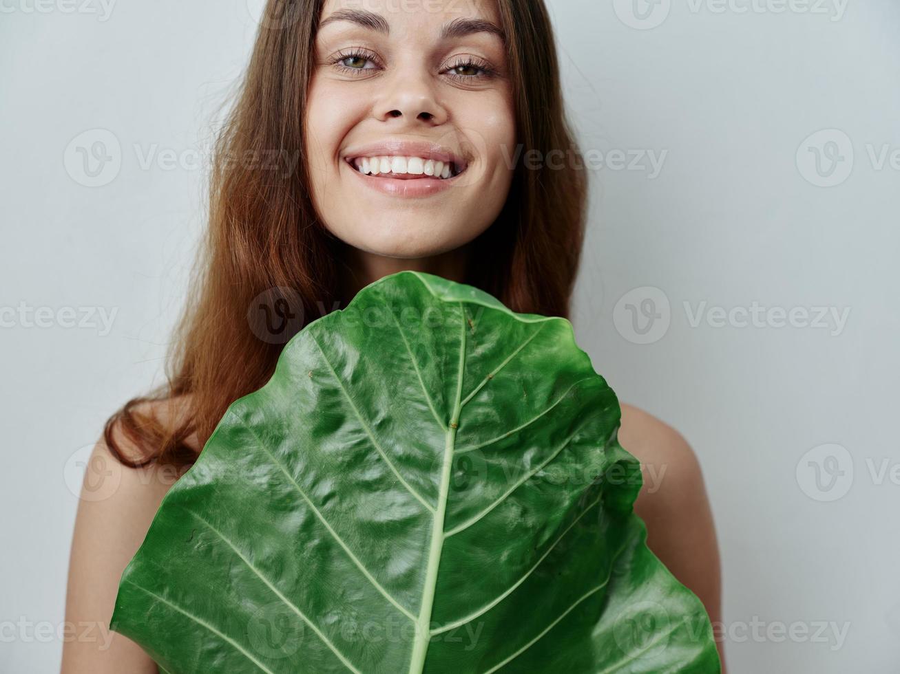 sonriente mujer y halaga un verde hoja en frente de su desnudo espalda exótico foto