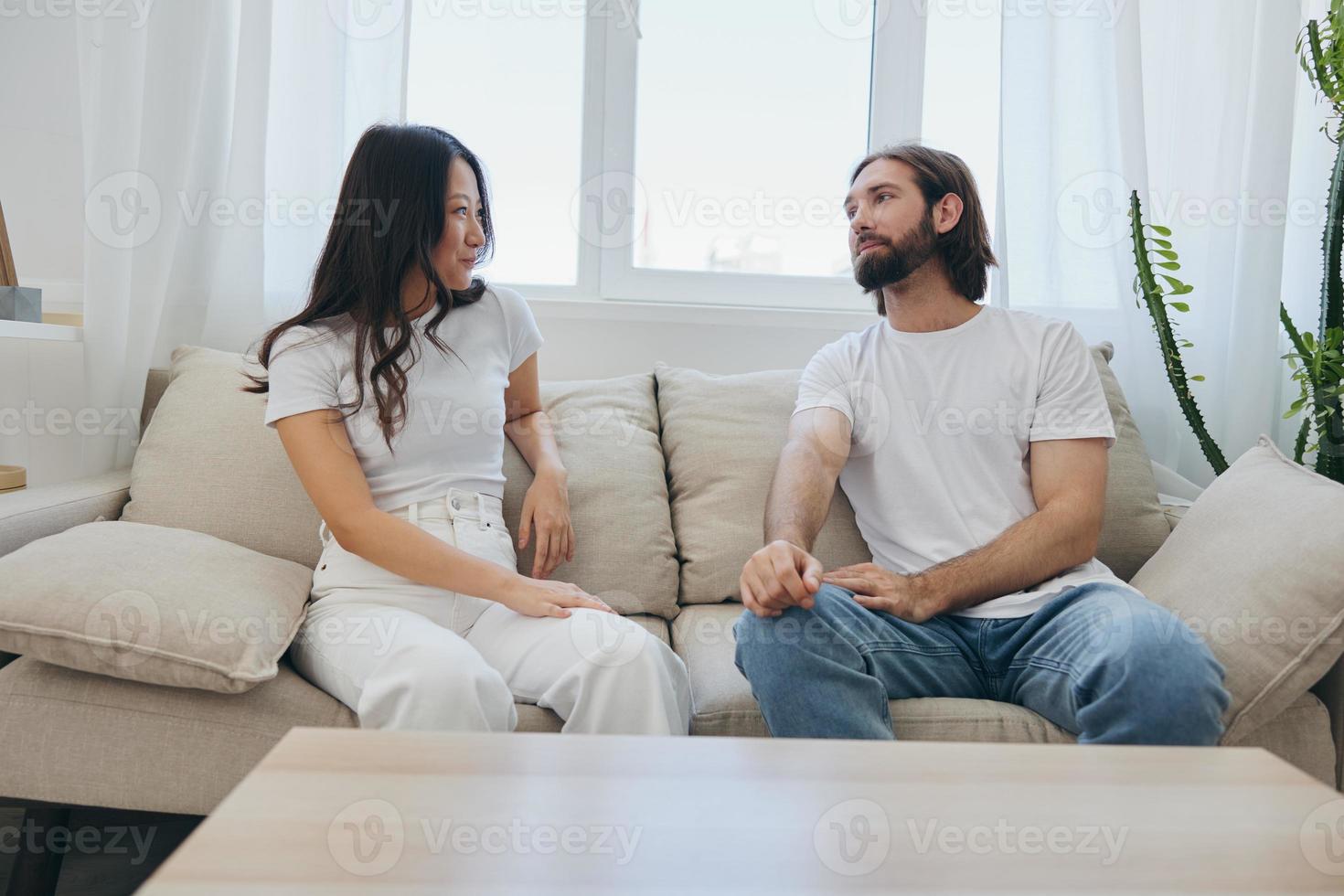 un hombre y un mujer sentado a hogar en el sofá en blanco elegante camisetas y chateando alegremente sonriente y riendo a hogar. masculino y hembra amistad foto