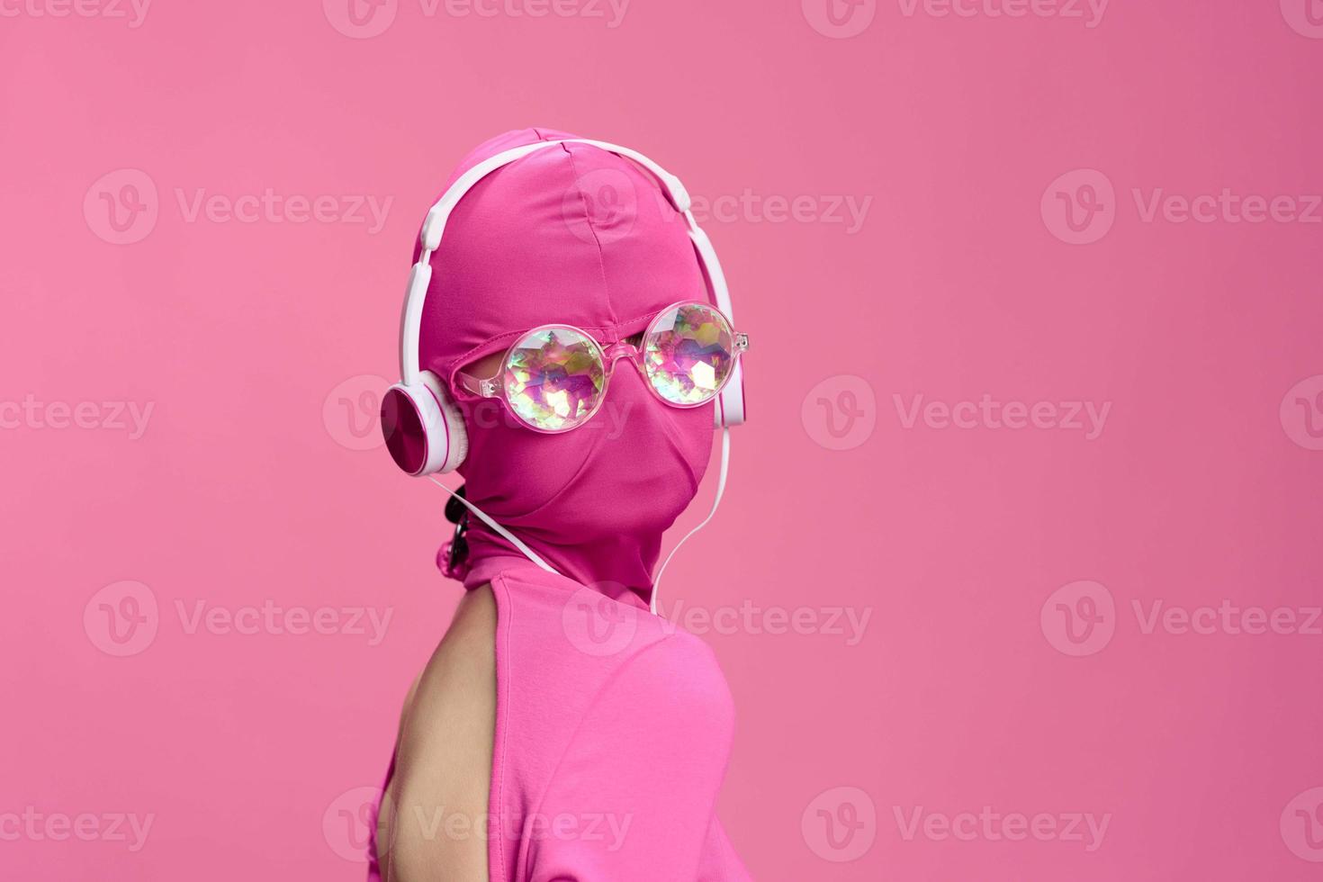 Creative fan art photo of a young female cyberpunk blogger on a pink background wearing a pink full-face mask with glowing round glasses and headphones