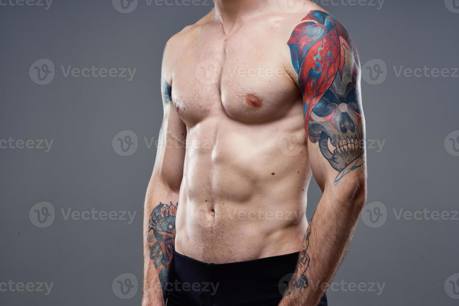 sporty man with pumped up abs tattoos on his arms gray background muscles photo