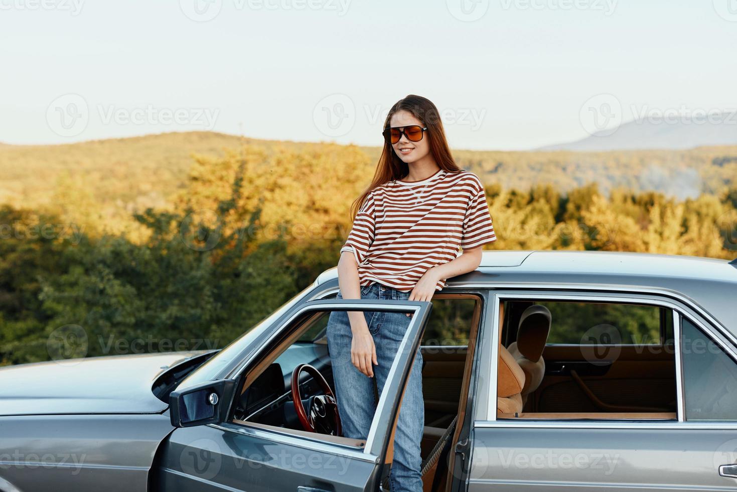 un joven mujer conductor mira fuera de el coche a el otoño paisaje y sonrisas satisfactoriamente foto