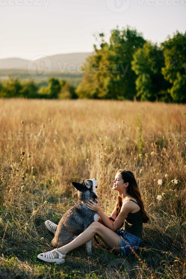 Woman sitting in field with dachshund dog smiling while spending time in nature with friend dog in autumn at sunset while traveling photo