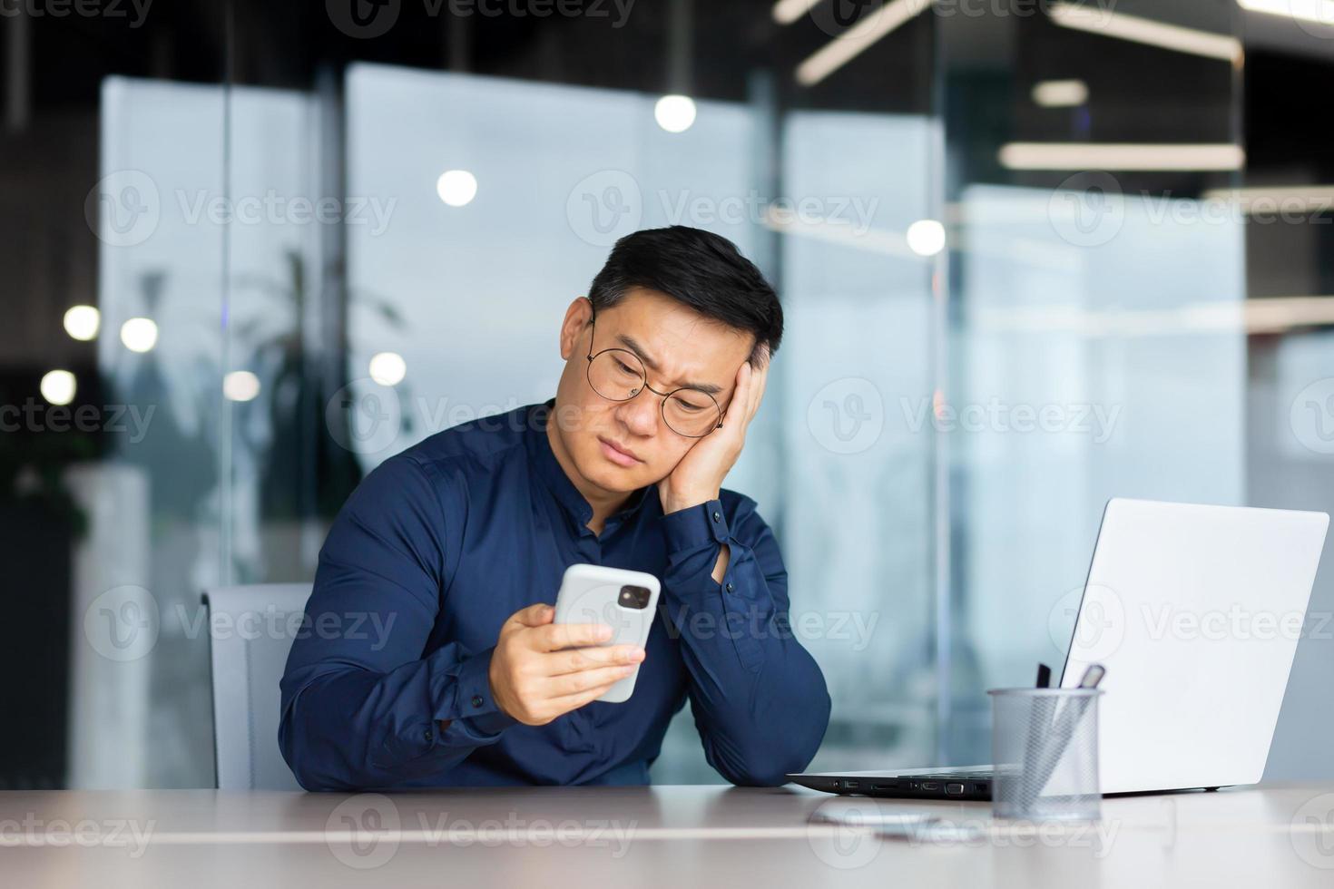 retrato de un preocupado joven asiático hombre mirando tristemente a el teléfono. aburrido, recibido malo Noticias foto